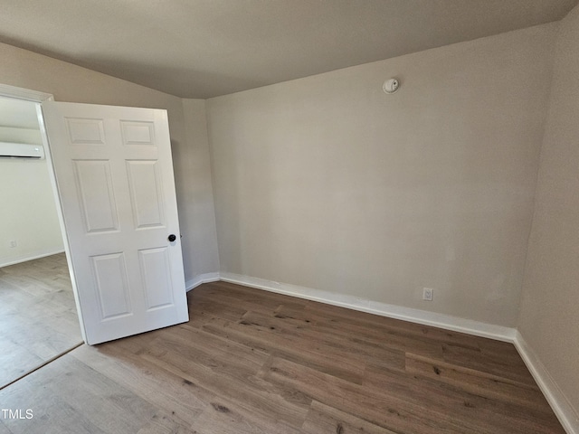 unfurnished bedroom with wood-type flooring and a wall mounted air conditioner