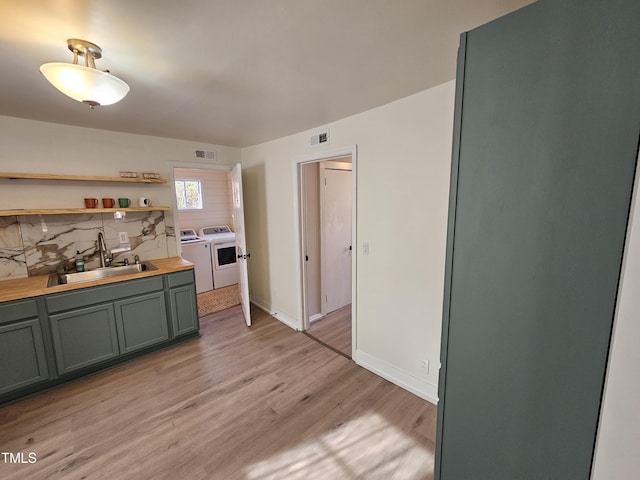 kitchen featuring sink, butcher block countertops, light hardwood / wood-style flooring, tasteful backsplash, and washer and dryer