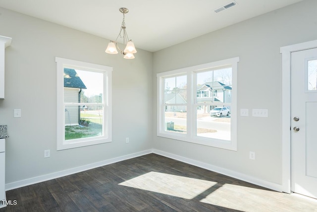 unfurnished dining area featuring an inviting chandelier, dark wood-type flooring, and plenty of natural light