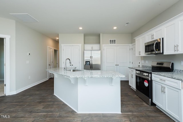 kitchen with appliances with stainless steel finishes, sink, white cabinets, light stone counters, and a center island with sink