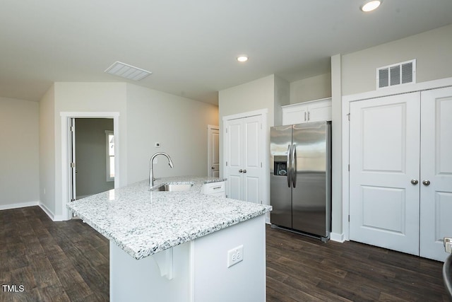 kitchen featuring sink, light stone counters, stainless steel fridge, a kitchen island with sink, and white cabinets