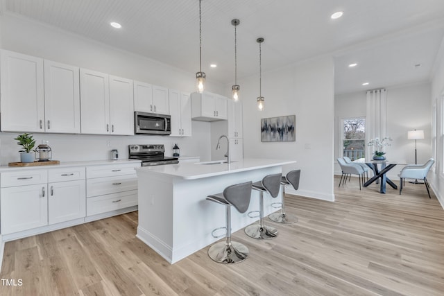 kitchen featuring pendant lighting, an island with sink, sink, white cabinets, and stainless steel appliances