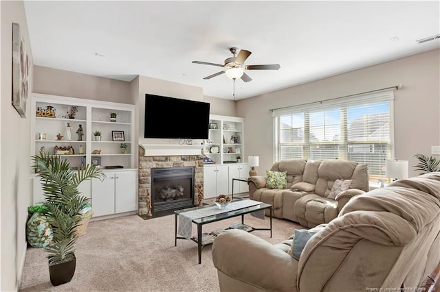 carpeted living room with a stone fireplace and ceiling fan