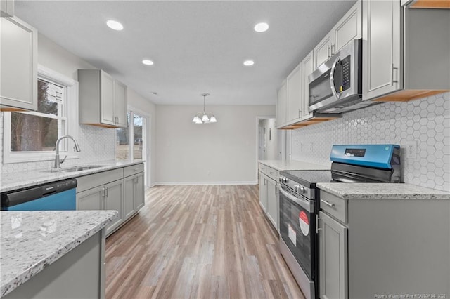 kitchen with light wood-type flooring, a sink, stainless steel appliances, baseboards, and light stone countertops