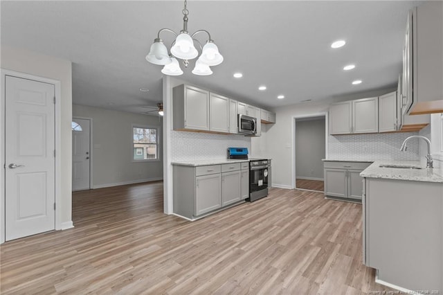 kitchen with light stone countertops, a ceiling fan, a sink, appliances with stainless steel finishes, and light wood-type flooring