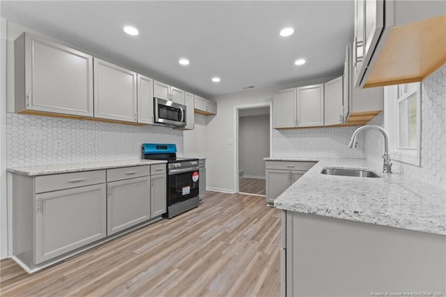 kitchen featuring light stone counters, light wood-style flooring, stainless steel appliances, and a sink