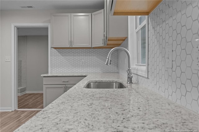 kitchen with visible vents, backsplash, light stone countertops, wood finished floors, and a sink