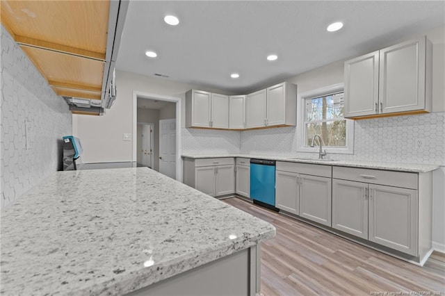 kitchen with backsplash, light stone counters, dishwashing machine, light wood-style floors, and a sink