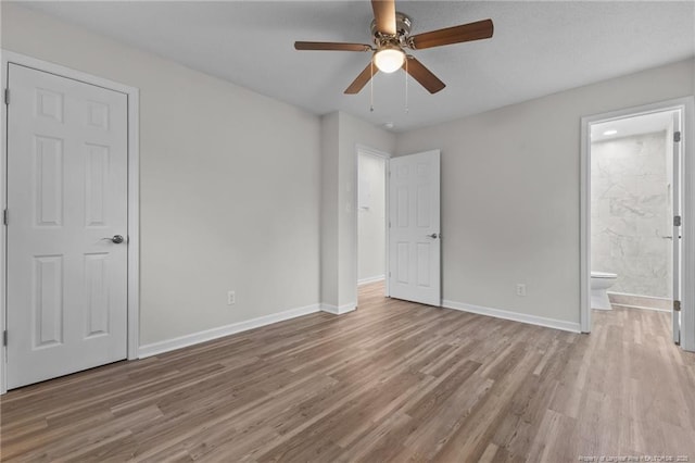 unfurnished bedroom with connected bathroom, a ceiling fan, baseboards, and wood finished floors