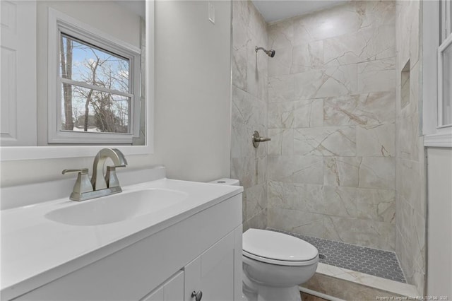 bathroom with tiled shower, toilet, and vanity