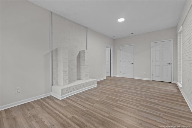 spare room with baseboards, brick wall, and light wood finished floors