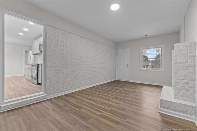 unfurnished living room with recessed lighting, baseboards, wood finished floors, and brick wall