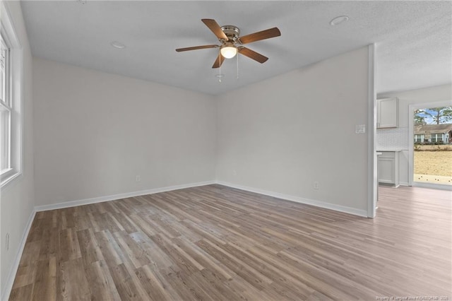 spare room with light wood-style flooring, a ceiling fan, and baseboards