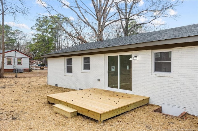 back of house featuring a shingled roof, brick siding, a deck, and fence