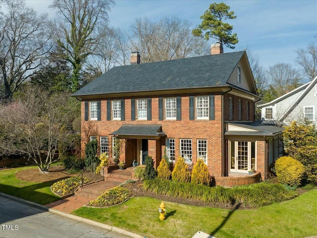 colonial house featuring brick siding, a chimney, and a front lawn