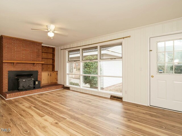 unfurnished living room featuring crown molding, a wood stove, ceiling fan, and light wood-type flooring