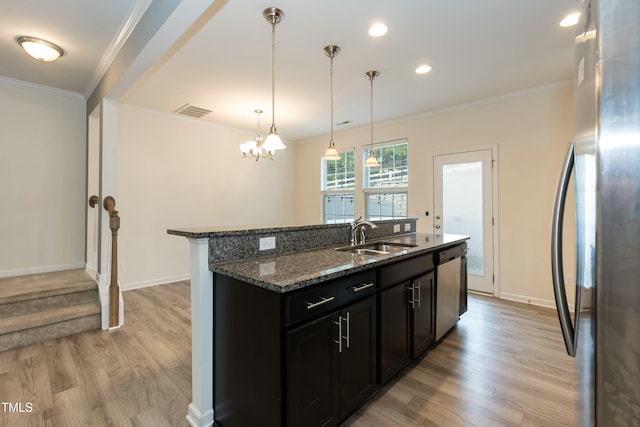 kitchen with sink, stainless steel appliances, a center island with sink, decorative light fixtures, and dark stone counters