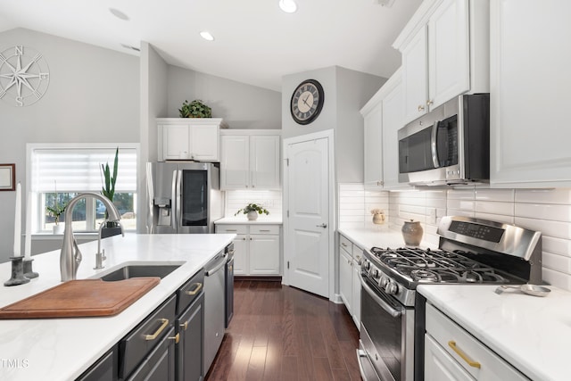 kitchen featuring stainless steel appliances, vaulted ceiling, sink, and white cabinets