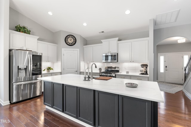 kitchen with stainless steel appliances, vaulted ceiling, a kitchen island with sink, and white cabinets