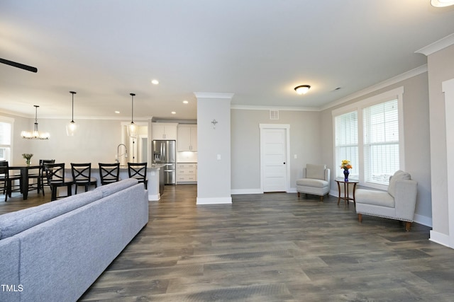 living room with a notable chandelier, crown molding, dark wood-type flooring, and sink