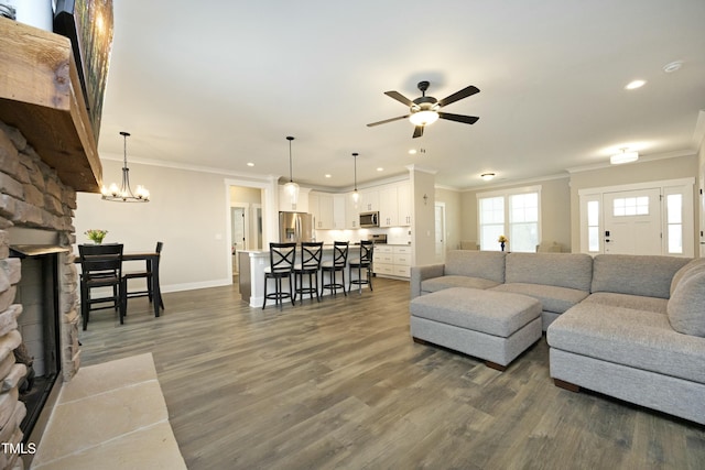 living room featuring dark hardwood / wood-style flooring, ornamental molding, ceiling fan with notable chandelier, and a fireplace