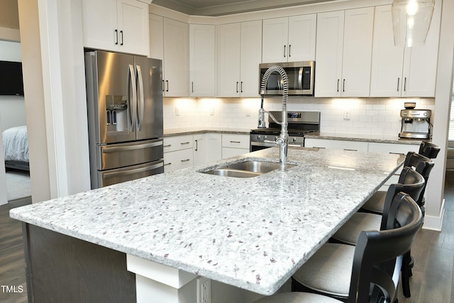 kitchen with a breakfast bar, appliances with stainless steel finishes, a kitchen island with sink, white cabinets, and dark hardwood / wood-style flooring