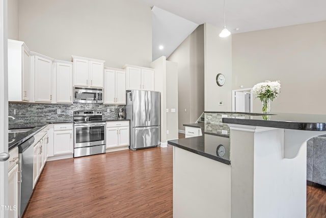 kitchen with high vaulted ceiling, stainless steel appliances, dark wood-style floors, tasteful backsplash, and dark countertops