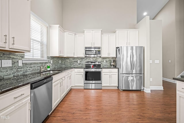 kitchen featuring stainless steel appliances, a towering ceiling, white cabinetry, a sink, and wood finished floors