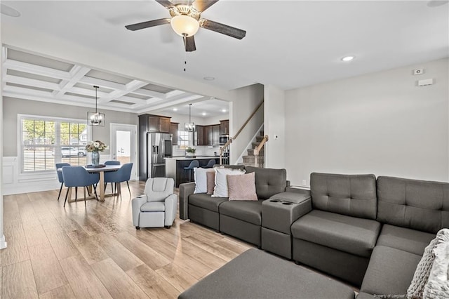 living room with coffered ceiling, ceiling fan with notable chandelier, beamed ceiling, and light wood-type flooring