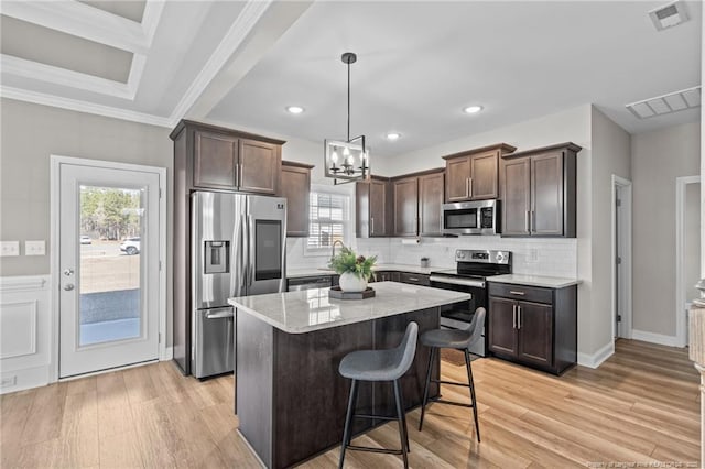 kitchen featuring appliances with stainless steel finishes, hanging light fixtures, a center island, dark brown cabinetry, and a kitchen bar