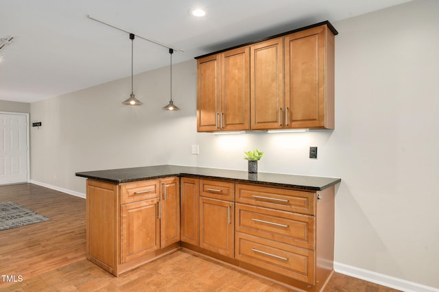 kitchen featuring dark stone counters, decorative light fixtures, kitchen peninsula, and light hardwood / wood-style flooring