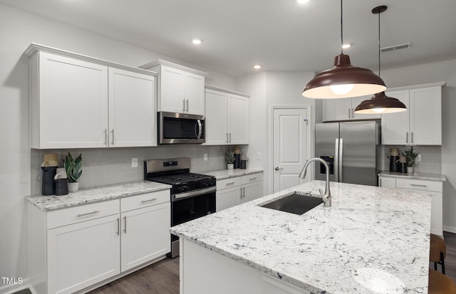 kitchen with sink, appliances with stainless steel finishes, an island with sink, pendant lighting, and white cabinets