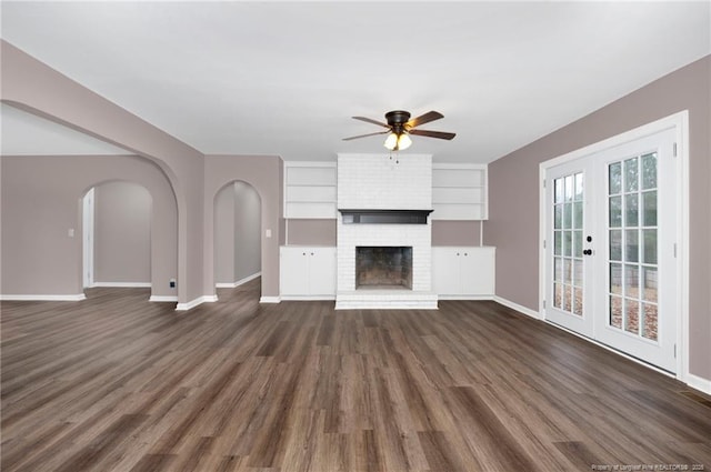 unfurnished living room with ceiling fan, dark wood-type flooring, a fireplace, and french doors