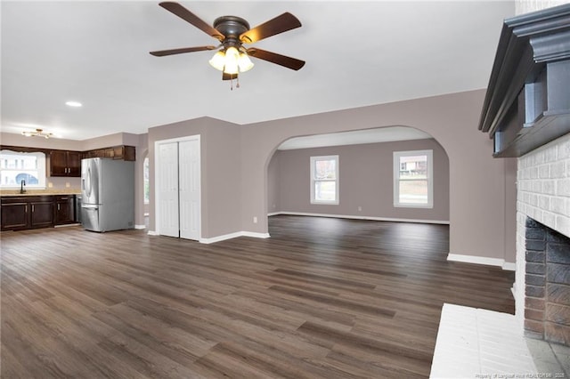 unfurnished living room featuring a brick fireplace, dark hardwood / wood-style floors, sink, and ceiling fan