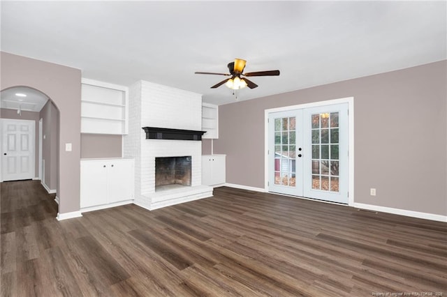 unfurnished living room featuring french doors, built in shelves, a brick fireplace, dark hardwood / wood-style floors, and ceiling fan