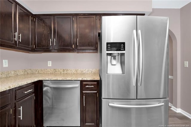 kitchen with dark hardwood / wood-style flooring, dark brown cabinets, light stone countertops, and appliances with stainless steel finishes