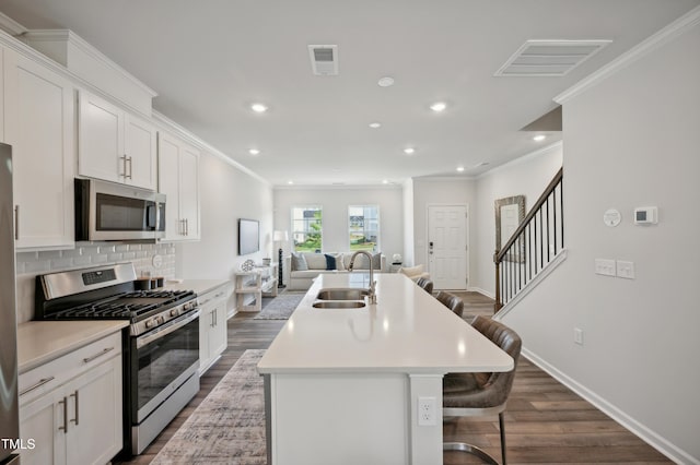 kitchen with sink, appliances with stainless steel finishes, a kitchen breakfast bar, an island with sink, and white cabinets