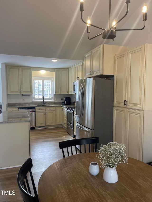 kitchen with light hardwood / wood-style flooring, stainless steel appliances, light stone counters, cream cabinets, and sink