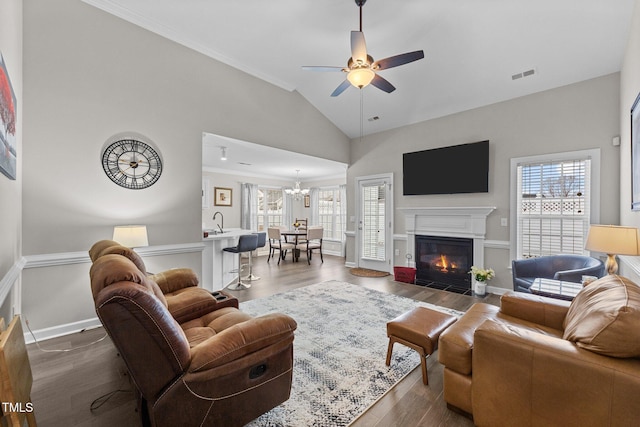 living area featuring ceiling fan with notable chandelier, a fireplace with flush hearth, visible vents, baseboards, and dark wood-style floors