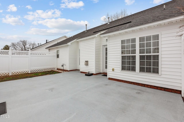 back of property featuring a shingled roof, a patio area, and fence