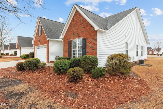 view of side of home with a garage, brick siding, roof with shingles, and central air condition unit