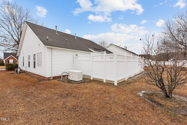 back of house featuring a yard, central AC unit, and roof with shingles