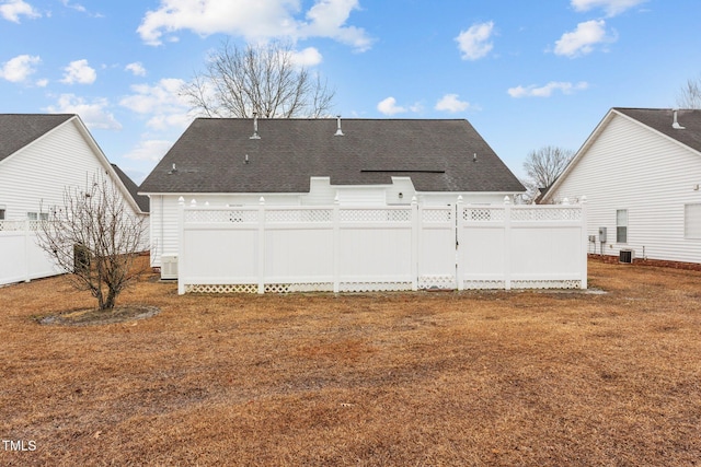 rear view of house featuring roof with shingles, a yard, and fence