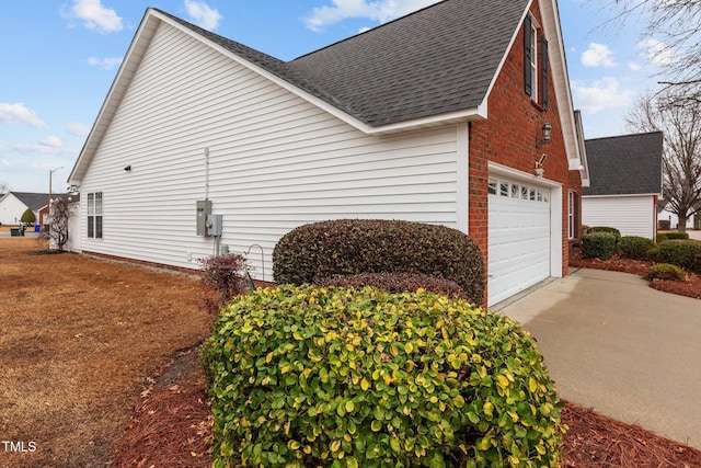 view of home's exterior featuring concrete driveway, roof with shingles, brick siding, and an attached garage