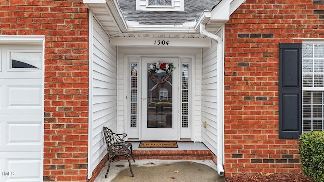 view of exterior entry with a shingled roof and brick siding