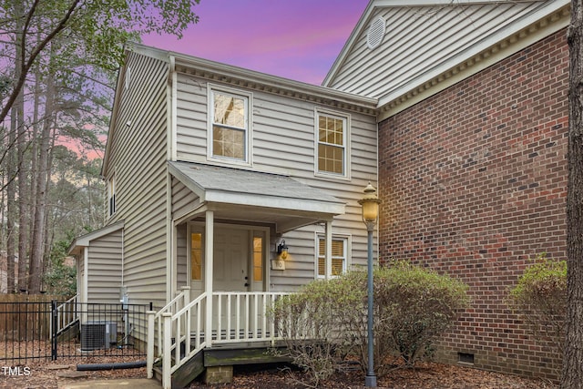 view of front of property featuring cooling unit, crawl space, brick siding, and fence