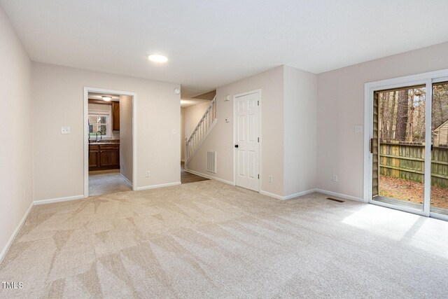 spare room with light colored carpet, visible vents, a sink, and stairs