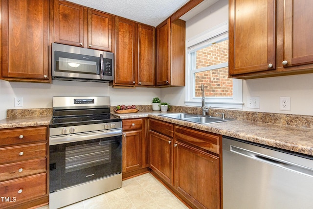 kitchen featuring a textured ceiling, stainless steel appliances, brown cabinetry, and a sink