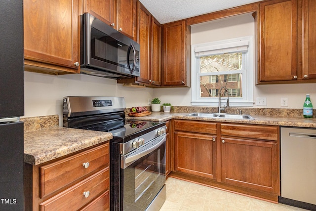 kitchen featuring brown cabinets, stainless steel appliances, a textured ceiling, light countertops, and a sink