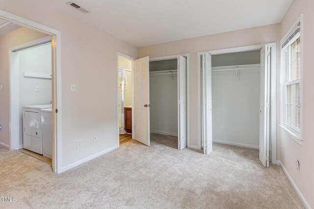 unfurnished bedroom featuring multiple closets, visible vents, light colored carpet, washer and dryer, and baseboards